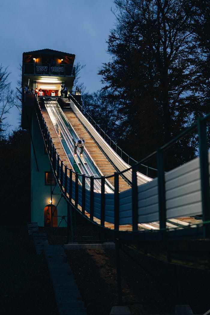 A ski jumper descending a lit ski jump ramp at night in Leutersdorf, Germany.